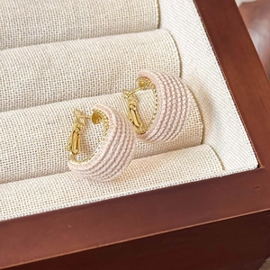 Macro shot of pink knitted fabric C-shaped earrings with gold metal base in a jewelry box