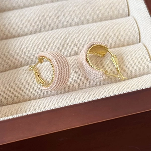 Close-up of pink knitted hoop earrings with gold metallic bead trim in a velvet box