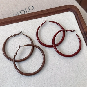 Close-up of brown and burgundy glossy hoop earrings displayed on a rustic wooden board