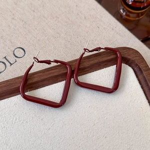 Macro shot of dark red square hoop earrings with a glossy lacquer finish on a wooden tray