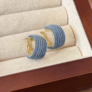 Detail shot of C-shaped blue denim earrings with gold metal accents on jewelry box