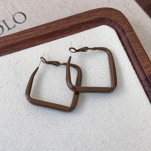 Close-up of geometric square brown earrings on a premium walnut wood display tray