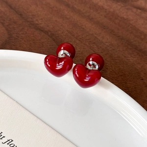 Detailed macro of cherry red heart-shaped earrings with glossy enamel finish on a ceramic plate