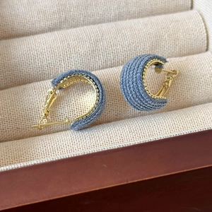 Close-up of blue fabric-wrapped C-shape earrings with gold beaded edges in a beige box