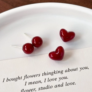 Close-up of deep cherry red heart and round ball stud earrings on a white plate