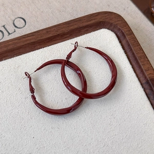 Macro view of dark red glossy hoop earrings on a vintage textured surface with pin closure