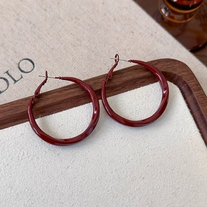 Close-up of deep red metallic hoop earrings on a textured off-white display surface