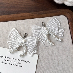 Détail de breloques papillon en dentelle blanche avec pompons en perles et fermoir