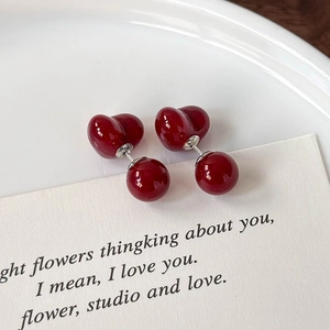 Macro shot of deep red heart-shaped cherry earrings on a white ceramic plate detail