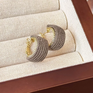 Detail of C-shaped fabric wrapped hoop earrings with golden needles on beige jewelry box