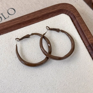 Macro shot of dark brown twisted hoop earrings with high-gloss mirror finish texture
