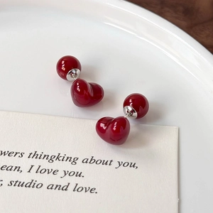 Macro view of glossy cherry red heart-shaped earrings with round ball backings on a tray