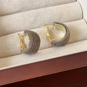 Close-up of gold C-shaped earrings with brown knit texture for a retro autumn style