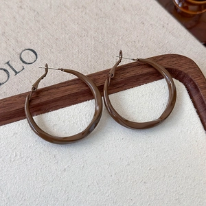 Macro detail of glossy brown coffee geometric twist hoop earrings on a textured tray