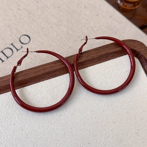 Macro shot of dark red hoop earrings with glossy finish on elegant beige fabric surface
