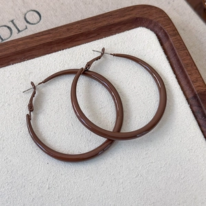 Detail of glossy brown geometric hoop earrings on textured white velvet background