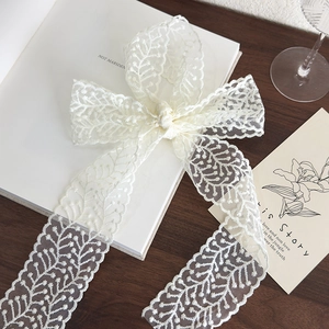 Close-up of a white vintage lace bow tie hair ribbon with detailed leaf-pattern weaving