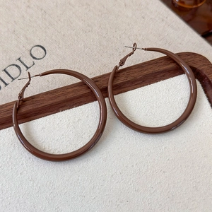 Detail of glossy dark brown geometric hoop earrings on a minimalist cream fabric background