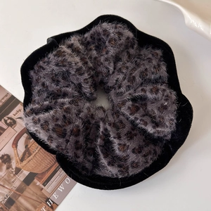 Detail of plush leopard print scrunchie with black velvet trim on minimalist background