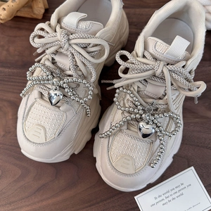 Pendentif cœur et nœud argenté sur baskets beiges à semelles compensées et lacets tressés