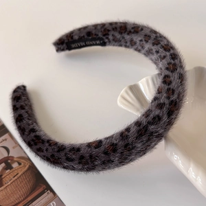 Detailed close-up of a grey leopard plush headband with a woven HAND MADE label