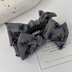 Gros plan sur la pince à cheveux en tissu gris avec motifs de nœuds noirs sur fond neutre