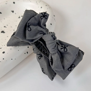 Détail de la pince à cheveux grise à nœuds superposés avec motifs papillons sur plateau