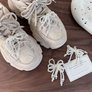 Beige chunky platform sneakers featuring decorative pearl bow charms and woven laces