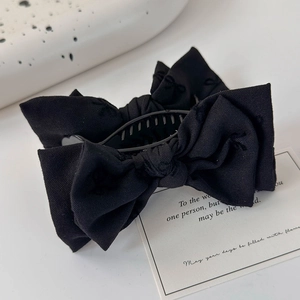 Détail de la pince à cheveux à nœud noir en tissu mat sur un fond de style minimaliste