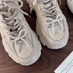 Vista dall'alto di sneakers chunky crema con eleganti ciondoli per scarpe con fiocco di perle