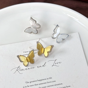 Macro shot of silver and gold brushed butterfly stud earrings on textured card