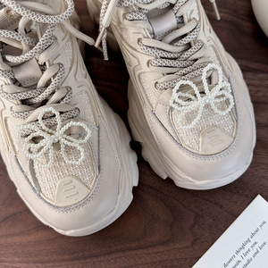 Dettaglio ravvicinato di sneaker beige con eleganti ciondoli a fiocco di perle