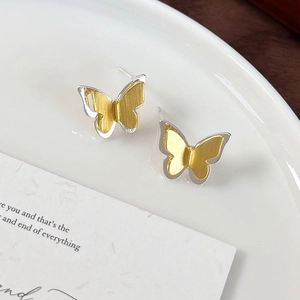 Close-up of textured gold and silver butterfly stud earrings on white ceramic