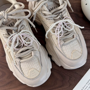 Dettaglio di ciondoli a fiocco con perle su lacci di sneakers beige con marchio Camel