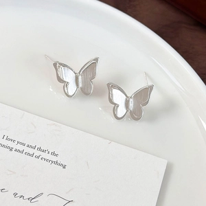 Macro shot of silver brushed metal butterfly stud earrings on a white porcelain tray