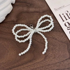 Detail of a handmade pearl bow charm with a silver lobster clasp for shoe decoration