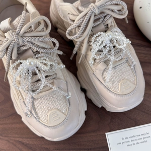 Detail of beaded pearl bow charms on beige chunky sneakers with lace-up decoration