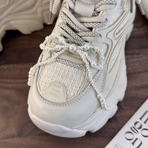 Close-up of DIY pearl bow charm attached to creamy white platform sneaker with lobster clasp