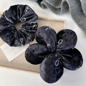 Close-up of black velvet hair scrunchie set with silver bow patterns on display tray
