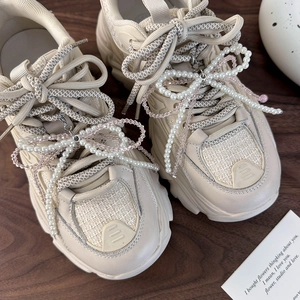 Dettaglio di accessori con fiocco di perle e ciondoli su sneakers beige con plateau