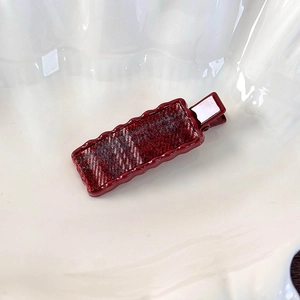 Détail de la texture du tissu à carreaux rouge sur une pince à cheveux vintage ondulée
