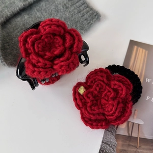 Détail d'une pince à cheveux rose tricotée rouge et d'un chouchou avec étiquette dorée