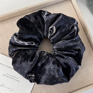 Close-up of a black velvet scrunchie with white hand-drawn bow and polka dot patterns