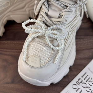 Close-up of pearl and crystal beaded bow accessory on cream platform sneakers