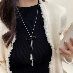 Long silver chain necklace with black bow and ballet shoe pendants on white tweed coat