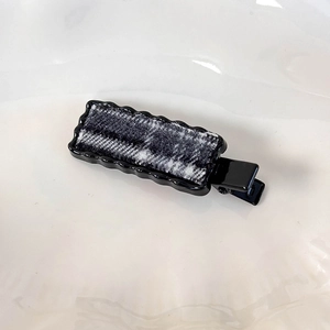Détail macro de l'insert en tissu écossais et bords ondulés sur une pince à cheveux collège