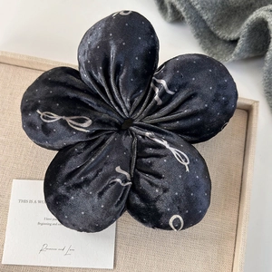 Close-up of black velvet flower scrunchie with silver bow and dot print on a tray
