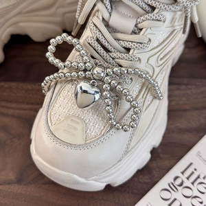 Detail of beaded bow charm and heart pendant on beige chunky platform sneakers