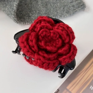 Détail de la rose rouge tricotée sur une grande pince à cheveux noire avec emblème