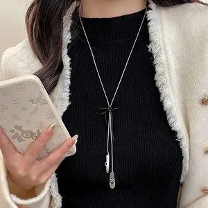 Detail of ballet slippers pendant and black bowknot on long silver sweater chain